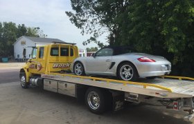 Bock's Service yellow flat-bed hauling truck loaded with a small sports car