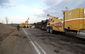 Multiple heavy-duty tow trucks winching up a turned-over semi