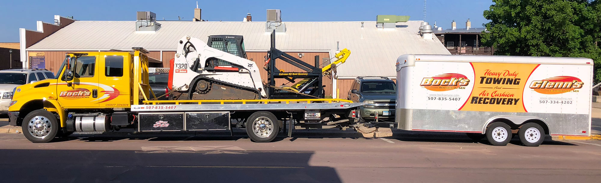 Bock's Service flatbed tow truck hauling a skid loader with a winch attachment used for off road recovery of equipment